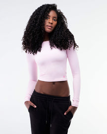 Woman wearing a pink long-sleeve crop top and black pants on a white background