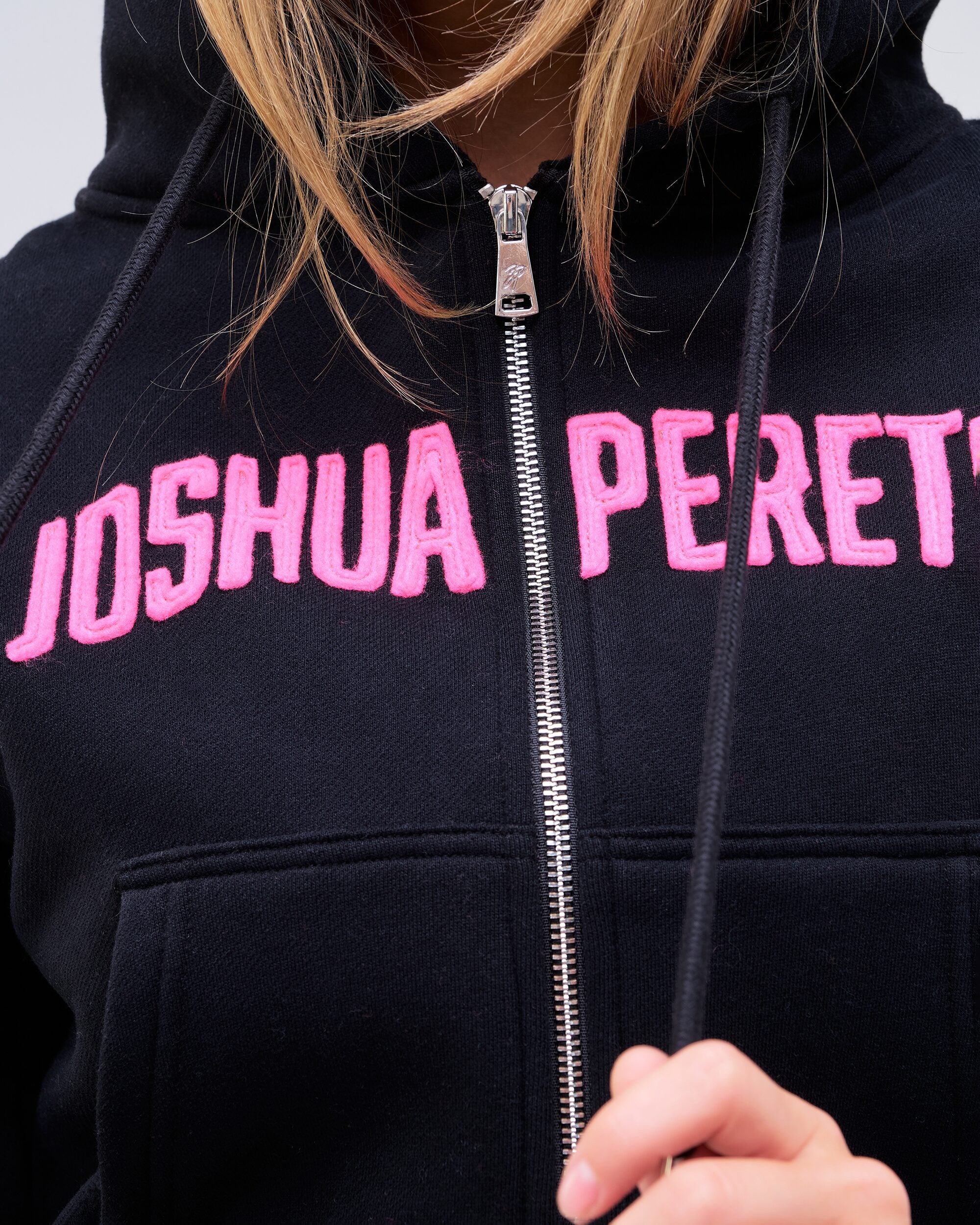 Paige relaxed-fit zip-up hoodie in black with pink logo, close-up of logo and zip